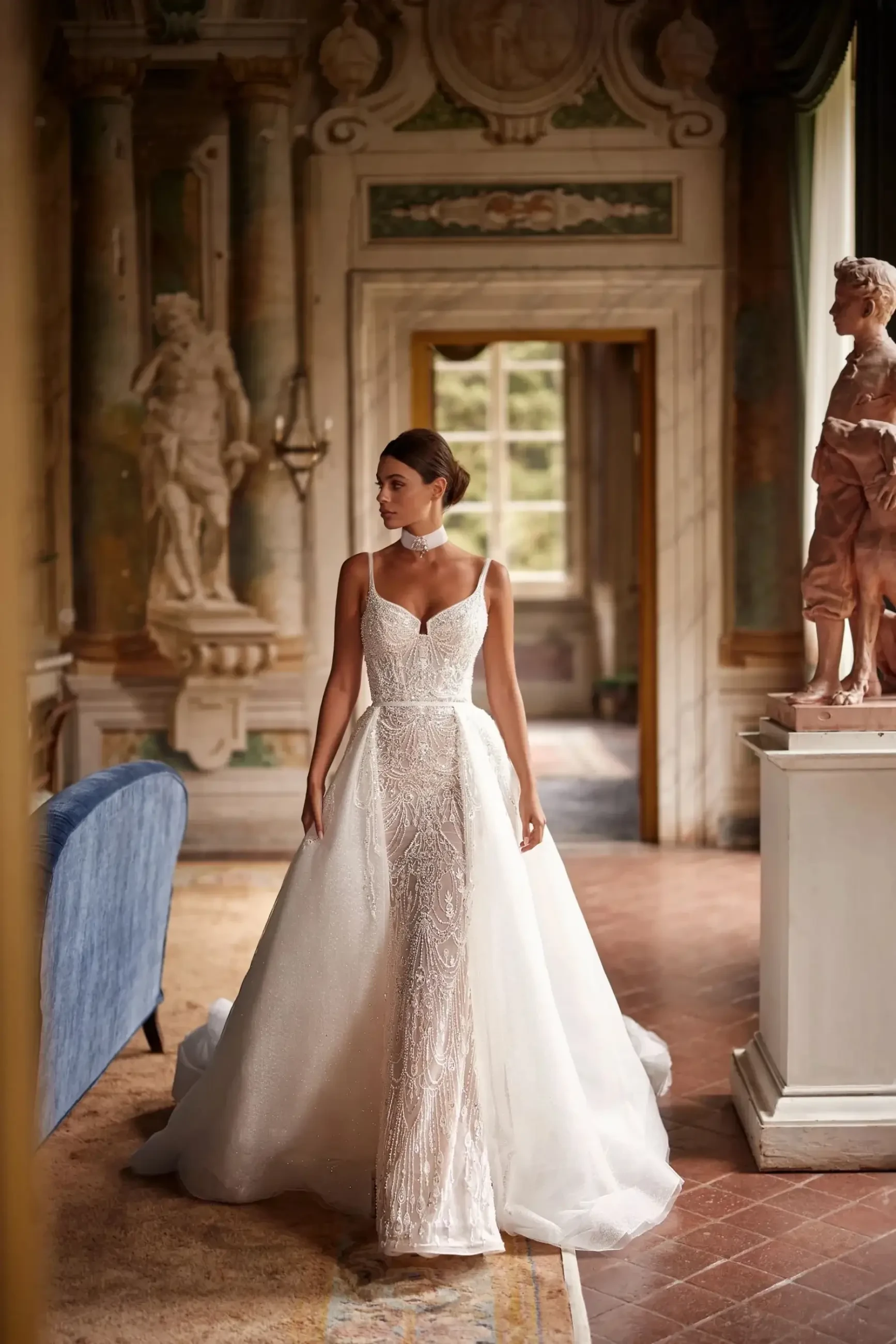 model is wearing a sleeveless beaded sheath wedding gown with a detachable overskirt