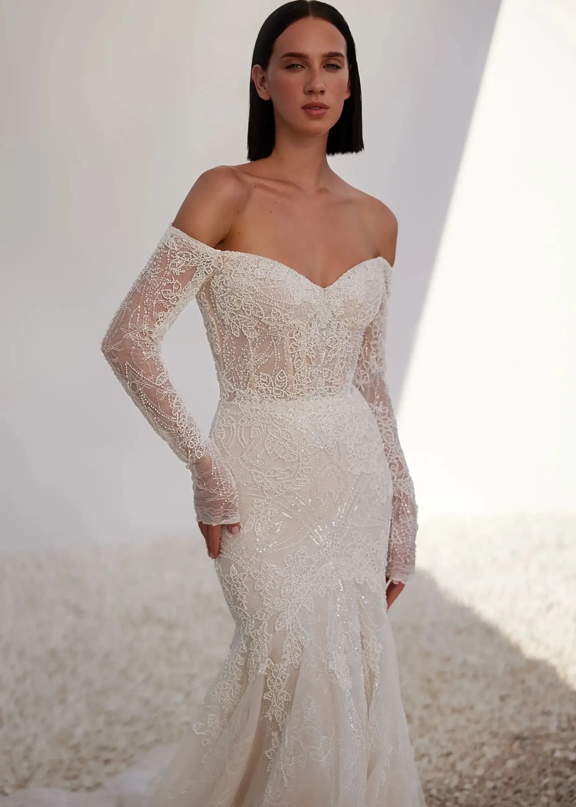 model is wearing a beaded off the shoulder long sleeve fit and flare bridal gown