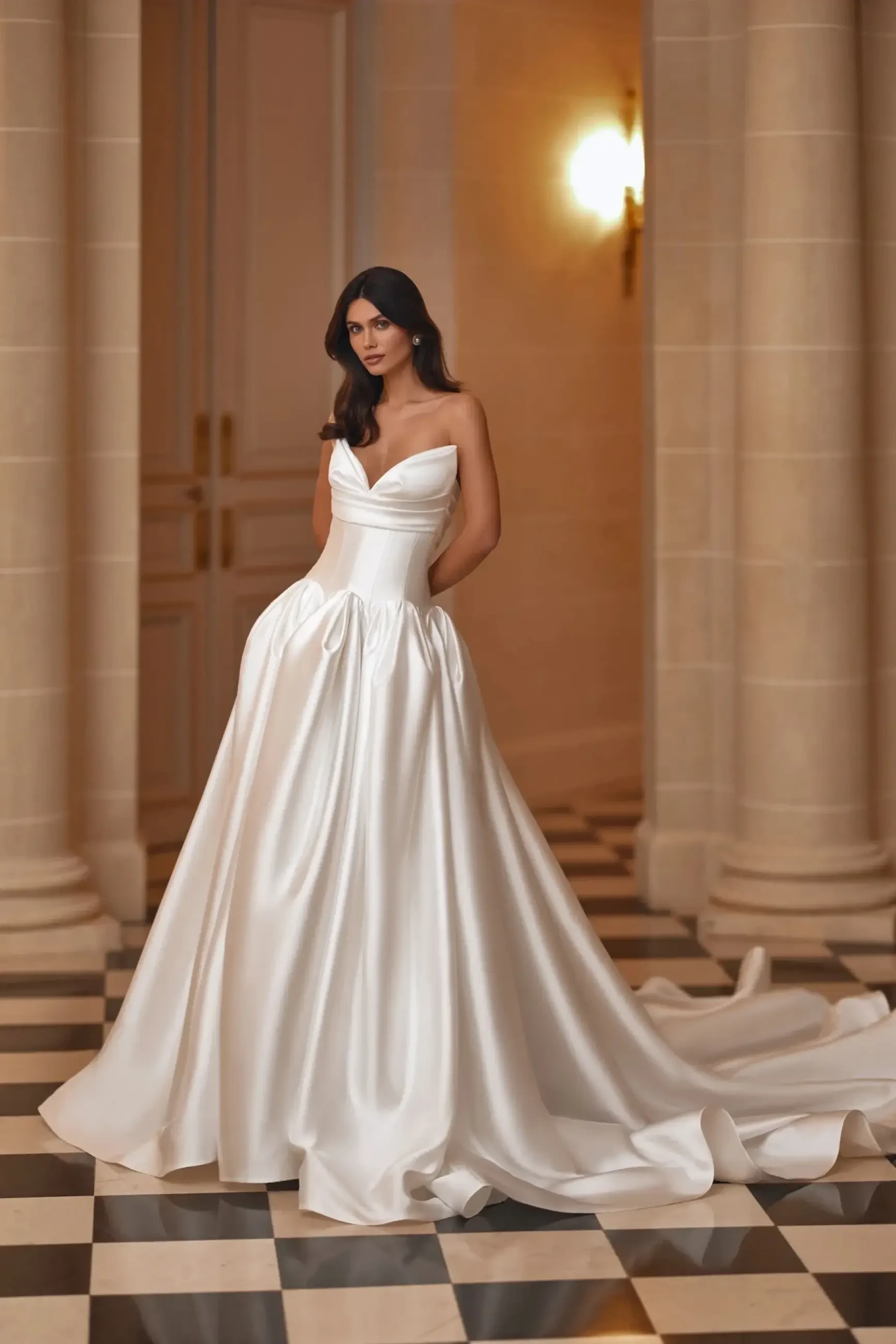 A woman wearing a strapless white gown stands on a checkerboard floor, with elegant architecture in the background.