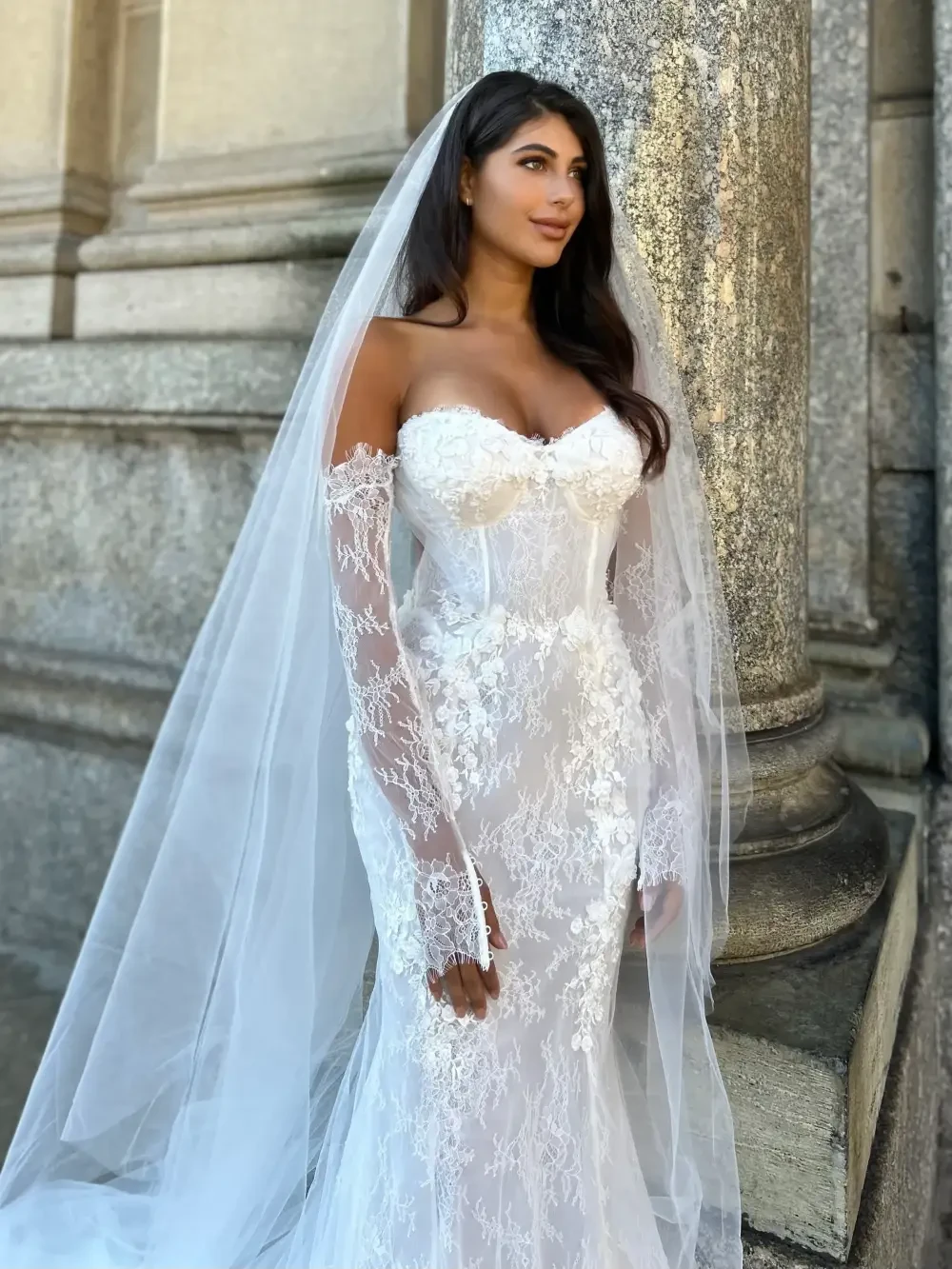 A woman in an elegant white wedding dress with intricate lace details and a long veil.