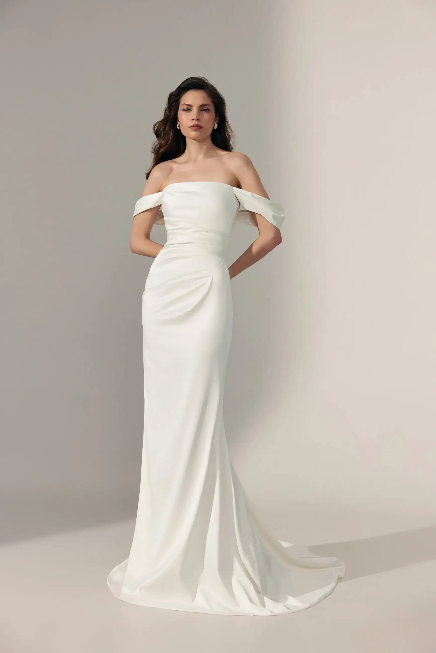 model is wearing an off the shoulder sheath wedding gown